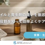 洗面台に置かれた透明なオイルの小瓶と細身のノズル付きボトル、木のくしとたたんだタオルが並ぶ静物イメージ