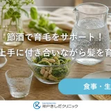 木のテーブルに小ぶりのグラスと炭酸水のボトル、豆と野菜を盛った小皿を並べた落ち着いた静物イメージ