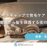 寝室のベッドサイドに、たたんだシルクのナイトキャップと木製のコーム、白いリネンが並ぶ静物イメージ