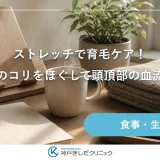 窓辺のデスクに木製のブックスタンドとノート、湯気の立つマグカップ、たたんだひざ掛けが並ぶ静かな静物イメージ