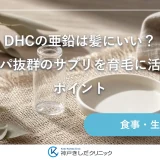 明るい室内の木のテーブルに麻のクロスを敷き、透明なガラスの小瓶と白い陶器の小皿、乾いた葉、リネンのナプキンを並べた静物イメージ