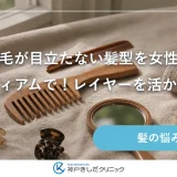 窓辺の台に並べた木製のコームとヘアクリップ、小さな手鏡、たたんだリネン布の静物イメージ