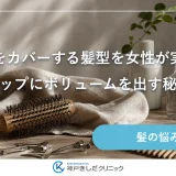 明るい洗面台に木製のロールブラシとドライヤー、たたんだ生成りのタオル、小さなヘアクリップが並ぶ静かな静物イメージ